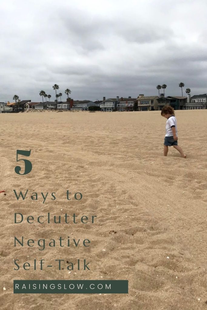 Small child walking on cloudy beach with houses in the background. Text overlay: 5 Ways to Declutter Negative Self-Talk, Raisingslow.com