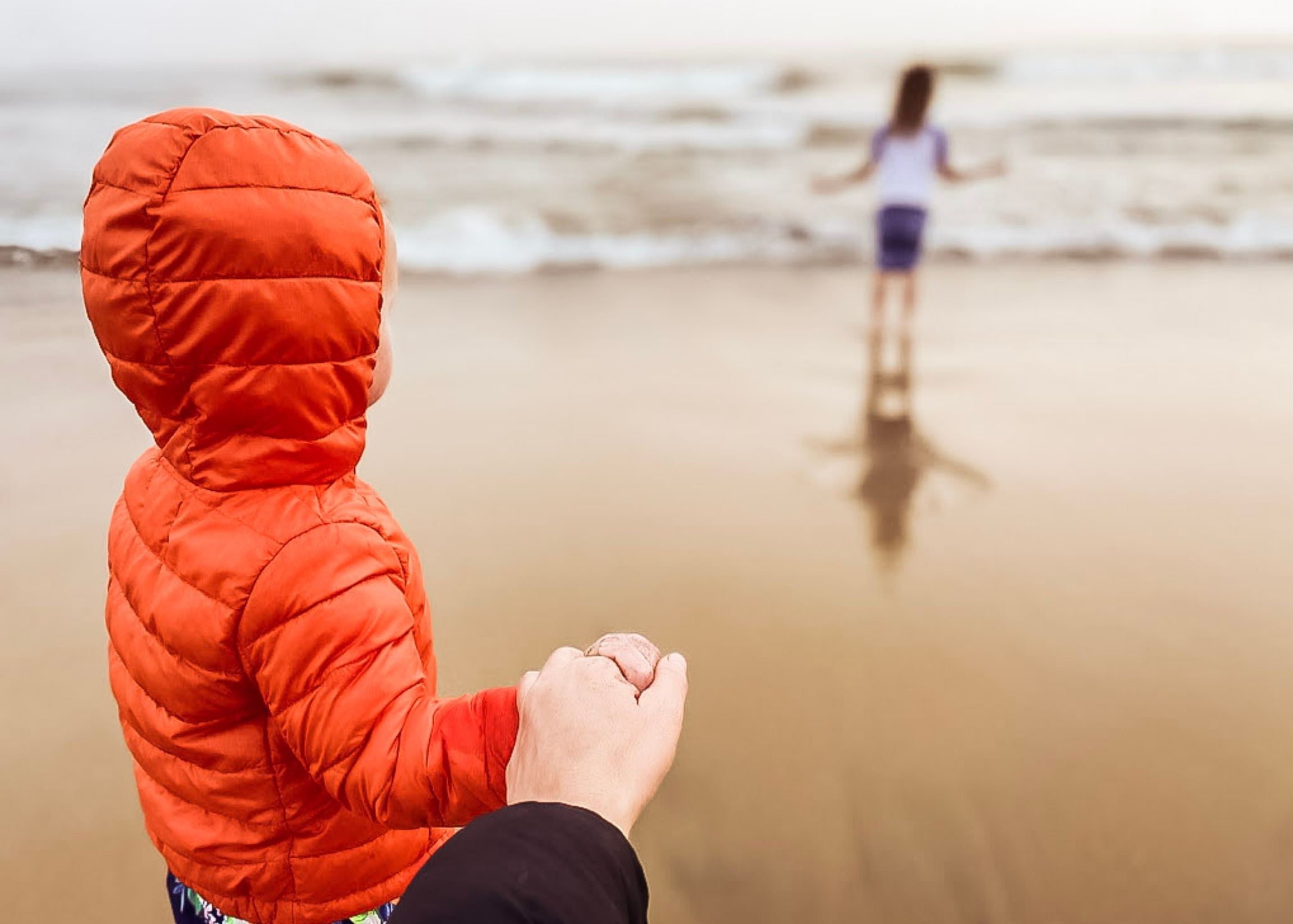 Mother holding child's hand, watching another child at the beach