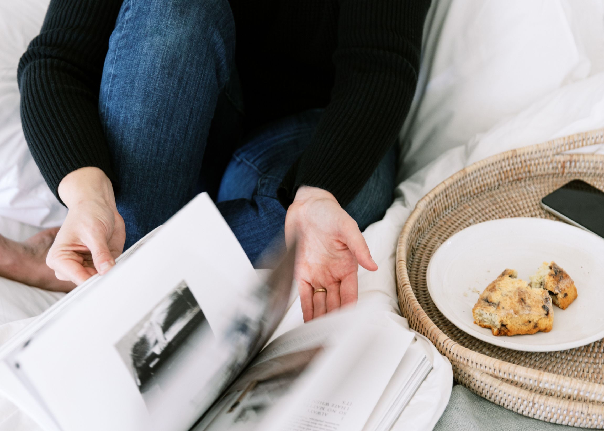 Woman flipping through magazine, on bed, with breakfast